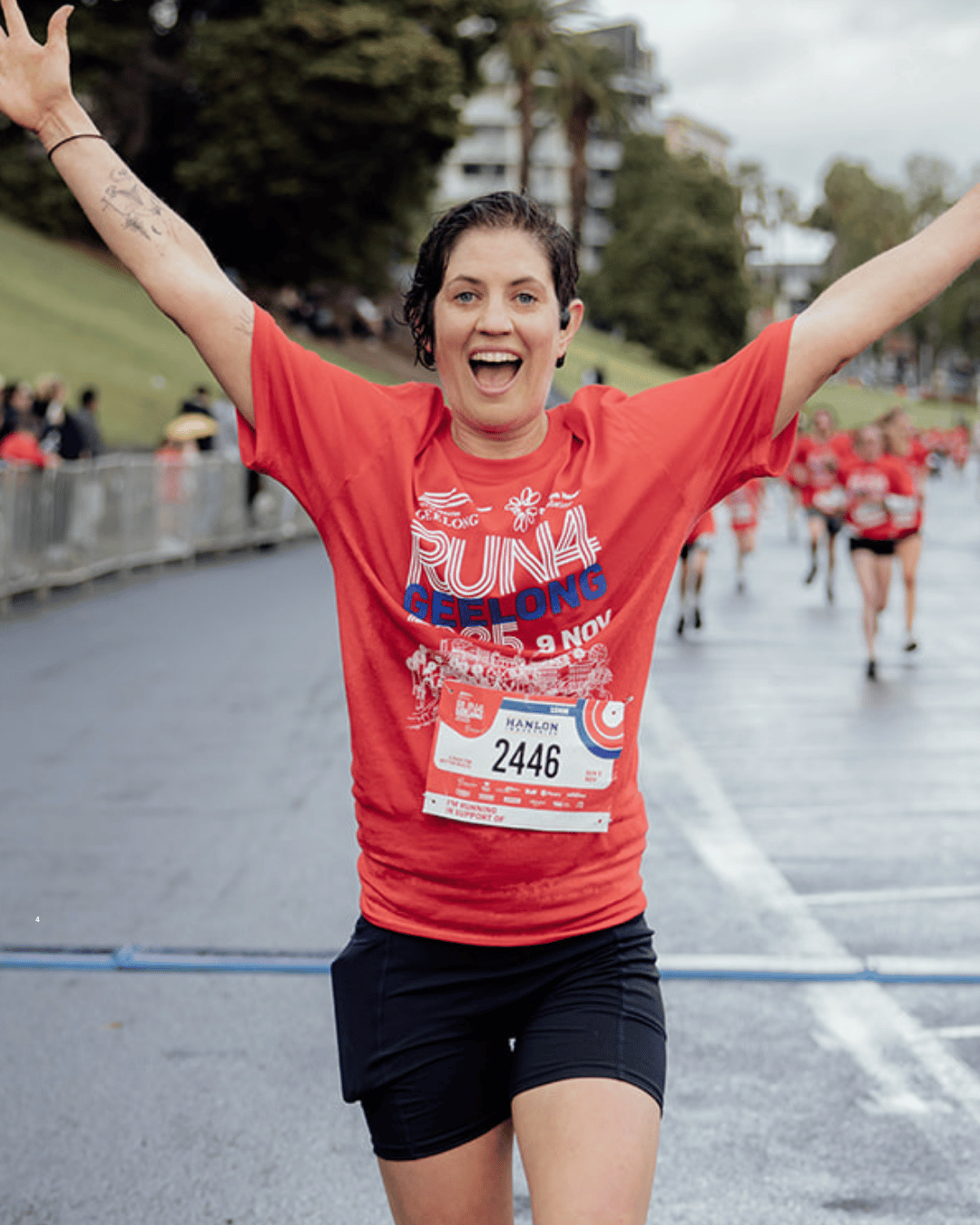 A runner crossing the Run4Geelong finish line with arms out, smiling
